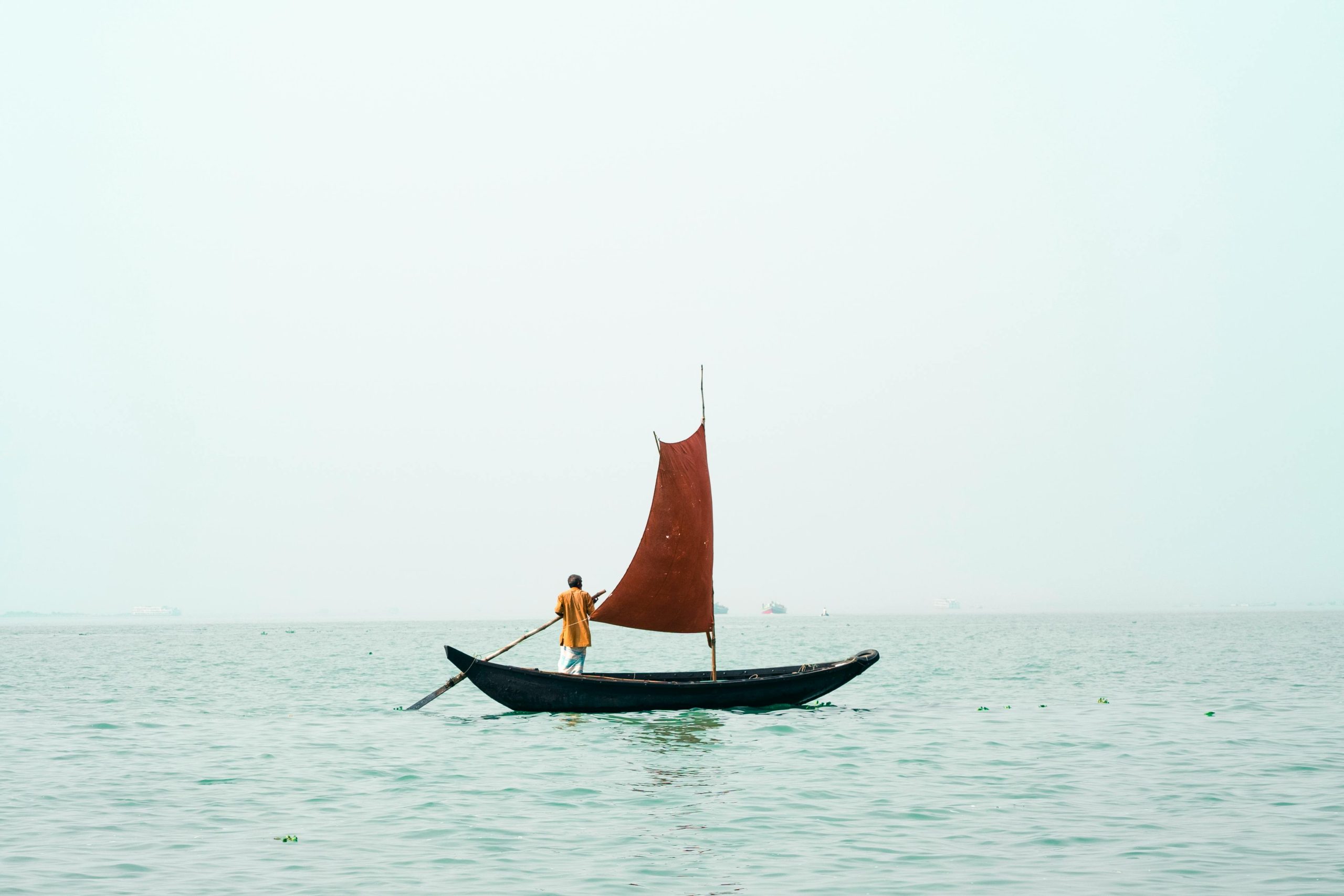 A lone fisherman sails a traditional boat on a serene Bangladesh waterway at sunrise.